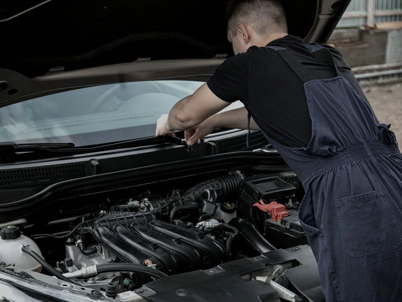 A mechanic in navy overalls leaning into an open engine bay outdoors