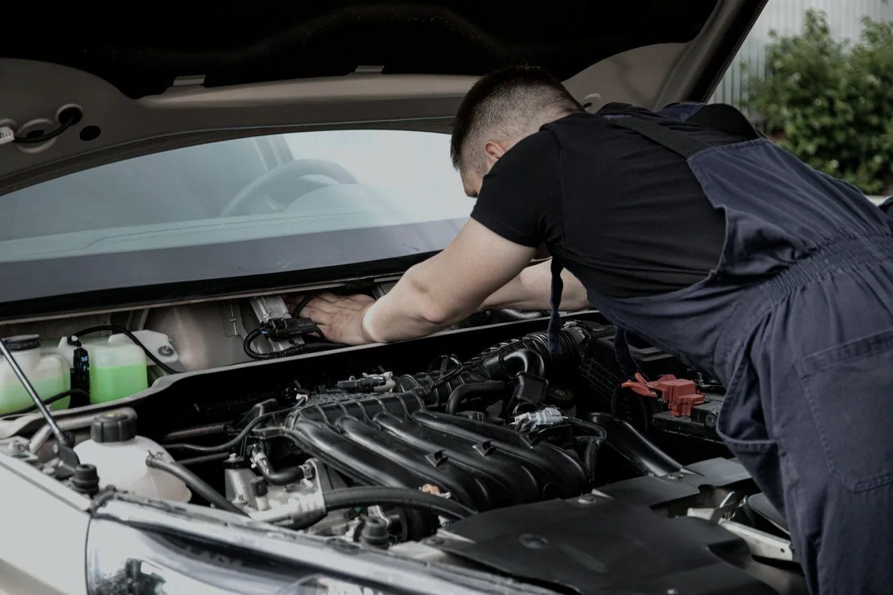 A mechanic working under an open bonnet on a driveway