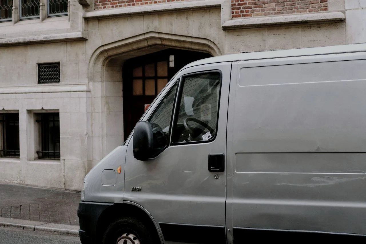 A white work van parked at the kerb beside a brick building
